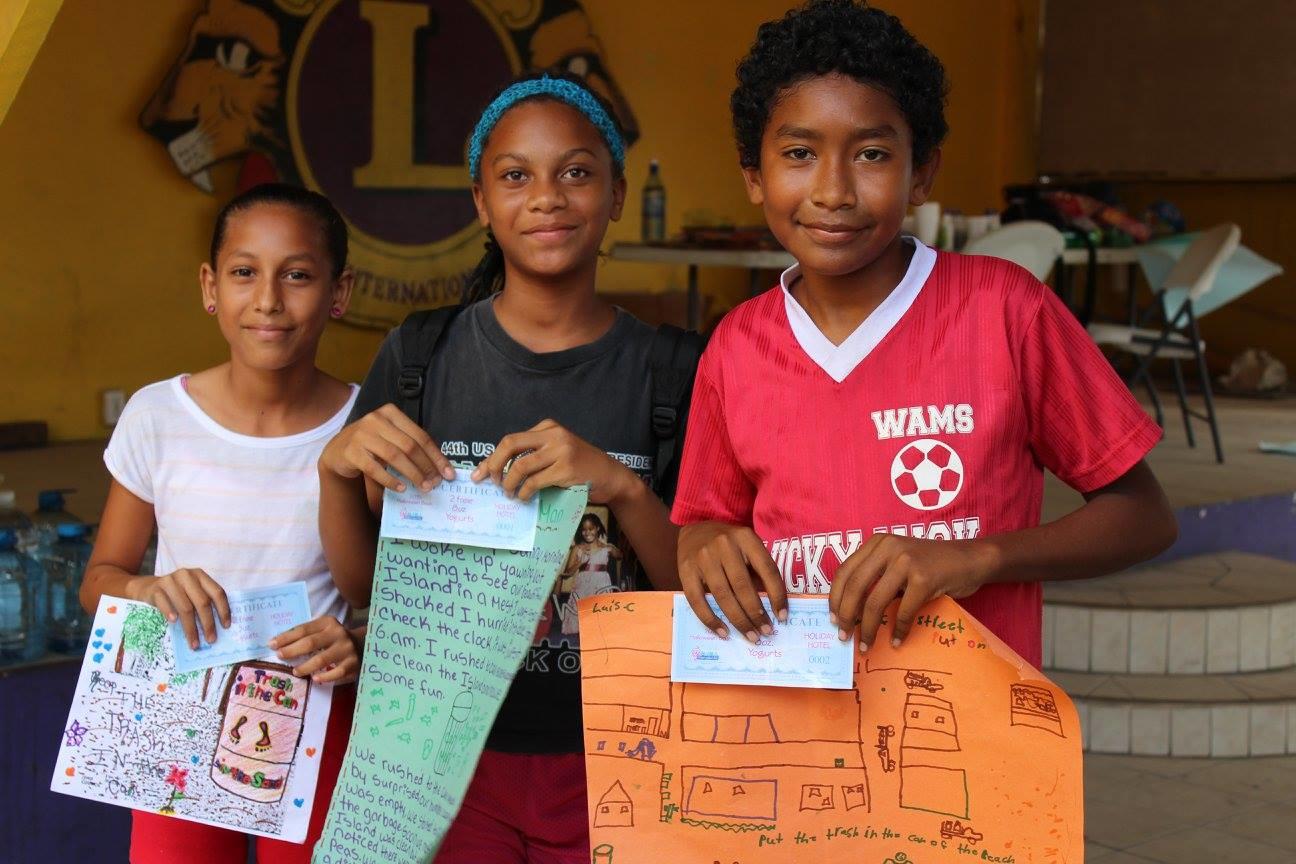 Three children in Belize show their certificates for participating in the Projects Abroad summer camp and illustrations of their work. A Projects Abroad volunteer working with children in Belize helps children celebrate with certificates they recieved for their hard work at a summer camp.